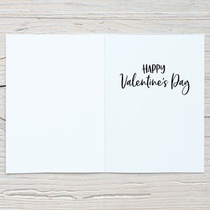 May include: A blank white card with the text "Happy Valentine's Day" written in black cursive on the right side of the card.
