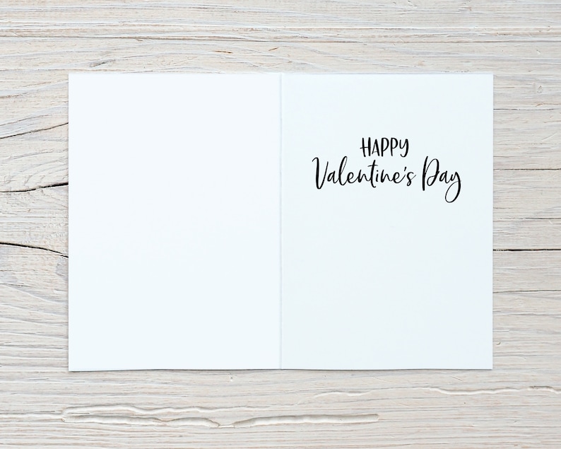 May include: A blank white card with the text "Happy Valentine's Day" written in black cursive on the right side of the card.