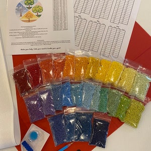 Pode incluir: Um kit de pintura de diamantes com contas de várias cores em sacos pequenos, dispostas em um espectro de arco-íris. Inclui ferramentas, uma bandeja e instruções impressas. O kit também contém um rastreador de temperatura e uma tela. O texto "Relax your body. Calm your mind & Soothe your spirit" é visível.