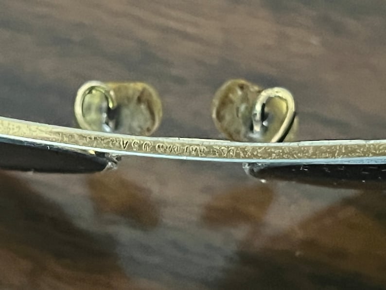 Peut inclure: Gros plan sur l'inscription "Ray-Ban USA" sur la monture en m&eacute;tal dor&eacute; d'une paire de lunettes de soleil.