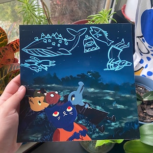 May include: A blue cat with red eyes and an orange shirt looks up at a dark blue sky with glowing constellations. The constellations include a whale, a bell, a fish, and a bird. The cat is surrounded by three other characters, including a fox, a red-headed character, and a grey creature with a long nose.