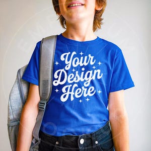 May include: A young person wearing a royal blue t-shirt with the text "Your Design Here" in white. The shirt has a distressed, vintage look. The person is wearing a grey backpack.
