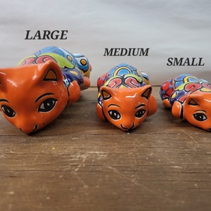 May include: Three ceramic cat figurines in different sizes, labeled "LARGE", "MEDIUM", and "SMALL". The cats are orange with colorful painted designs and black eyes.