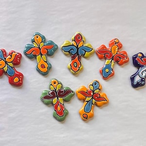Könnte beinhalten: Sieben farbenfrohe Keramik-Kreuze mit aufwendigen floralen Designs. Jedes Kreuz hat eine einzigartige Kombination aus Rot, Blau, Gelb, Orange und Grün mit glänzendem Finish. Diese dekorativen Kreuze sind ideal für religiöses Kunsthandwerk.