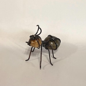 May include: A handcrafted metal ant sculpture with a brown and green body. The ant's head is a light brown colour, and the body segments are a darker green. The legs and antennae are made of thin, dark metal.