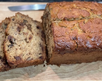 Può includere: Un pane di banana con gocce di cioccolato, tagliato a fette su un tagliere di legno.