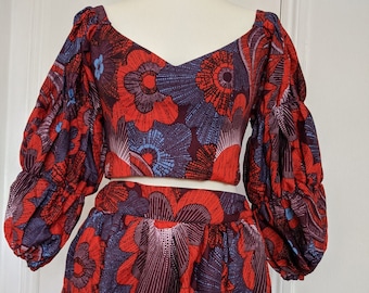 May include: A red and blue floral print crop top and skirt set. The top has a V-neck and puffed sleeves. The skirt is a midi length with a slit in the front.