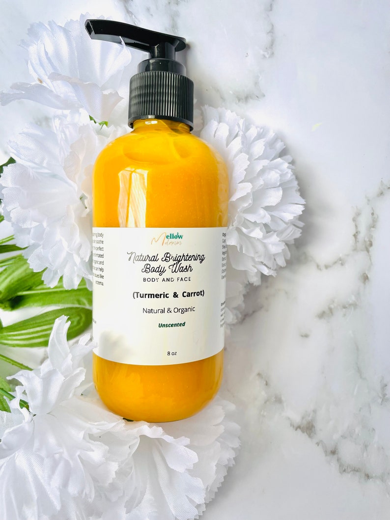 May include: A yellow bottle of Mellow Mama's Natural Brightening Body Wash with Turmeric & Carrot. The bottle is 8 oz and unscented. The bottle is on a white marble surface with white flowers.