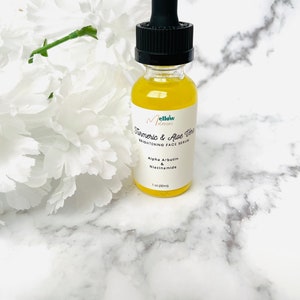 Puede incluir: Una botella de vidrio transparente con un gotero negro lleno de un l&iacute;quido amarillo. La etiqueta de la botella dice "Mellow Turmeric & Aloe Vera Brightening Face Serum" con los ingredientes "Alpha Arbutin & Niacinamide" y "1 oz (30ml)".