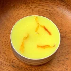 May include: A yellow candle with dried flower petals inside a silver tin.