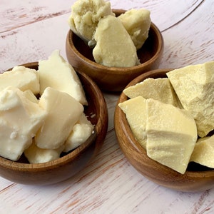 May include: Three wooden bowls filled with chunks of raw, unrefined shea butter. The shea butter is a light ivory color.
