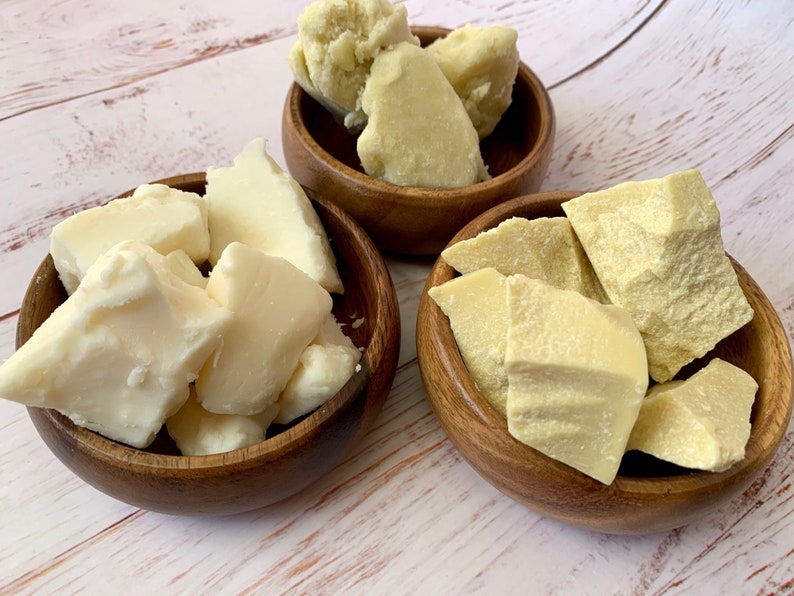 May include: Three wooden bowls filled with chunks of raw, unrefined shea butter. The shea butter is a light ivory color.