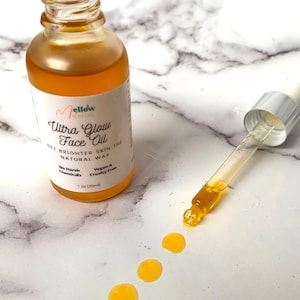 May include: A glass bottle of Mellow Ultra Glow Face Oil with a dropper. The bottle is labeled with the product name and ingredients. The oil is a light yellow color. The bottle is sitting on a white marble surface. Get brighter skin the natural way. No harsh chemicals. Vegan & cruelty free. 1 oz (30ml).