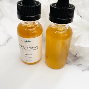 Pu&ograve; includere: Due bottiglie di vetro ambrato con tappi contagocce neri riempite di un liquido giallo chiaro. Le bottiglie sono etichettate "mellow interior Soothing & Calming Hydrating Face Serum Niacinamide & Oat Extract 1 fl oz (30ml)"