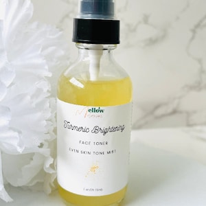 May include: A clear glass bottle with a yellow liquid inside. The bottle has a black spray top and a white label that says "Turmeric Brightening Face Toner Even Skin Tone Mist 2 oz (59 ml)".