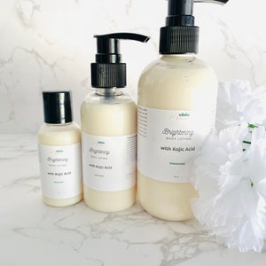 May include: Three bottles of body lotion with a pump dispenser. The bottles are labeled "Mellow Brightening Body Lotion with Kojic Acid". The smallest bottle is 1 oz, the middle bottle is 4 oz, and the largest bottle is 8 oz. The bottles are on a white marble surface.