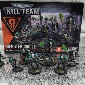 Op de afbeelding: Een Warhammer 40,000 Kill Team Hierotek Circle doosset met Necron Cryptek miniaturen. De set bevat diverse zwart en groen geschilderde robotachtige figuren met lichtgevende groene accenten, opgesteld voor de geïllustreerde productverpakking.