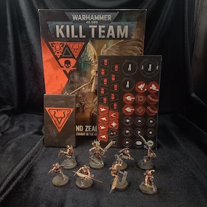 以下が含まれることがあります： Warhammer 40,000 Kill Teamのゲームセット。大きなゲームボックス、オレンジ色の雄牛のシンボルが描かれた小さな長方形のカードボックス、赤と黒のゲームトークンシート、円形の台座に乗った8体のミニチュアフィギュアが含まれています。