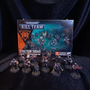 以下が含まれることがあります： 11体のシタデルミニチュアが入ったWarhammer 40,000 Kill Team Exaction Squadのボックスセット。箱には鎧を着た人物の暗い青緑色のイラストが描かれている。箱の前には、塗装された11体の兵士のミニチュアが並んでいる。