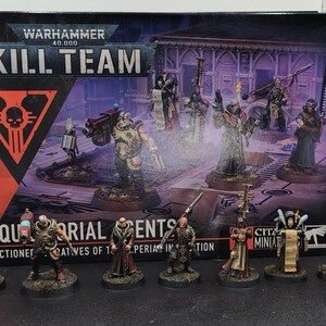以下が含まれることがあります： Warhammer 40,000 Kill Team Inquisitorial Agentsのボックスセットと、その前に並べられた7体の塗装済みミニチュアフィギュア。パッケージにはキャラクターのイラストとゲームタイトルがテキストで明記されています。