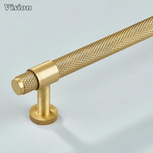 May include: Close-up of a gold-coloured cabinet pull with a diamond-patterned grip. The pull has a cylindrical bar and a round base. The word "Vision" is in the top left corner.