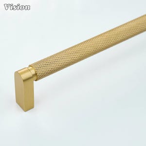 May include: A gold-coloured cabinet pull with a diamond-patterned handle and a right-angled end. The word "Vision" is in the upper left corner. This hardware is suitable for kitchen or bathroom cabinets.
