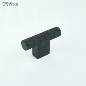 May include: A black cabinet pull with a textured, cylindrical handle and a square base. The word "Vision" is printed in white in the upper left corner. This modern hardware is suitable for drawers and cabinets.