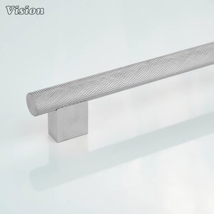 May include: A silver cabinet pull with a textured, cross-hatched design. The cylindrical handle is mounted on a square base. The word "Vision" is in the upper left corner.