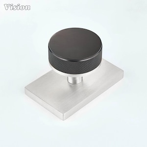 Pode incluir: Um puxador de móvel com topo circular preto de borda texturizada e serrilhada, sobre uma placa de base de metal prateado escovado. A palavra Vision está impressa no canto superior esquerdo. A ferragem possui um design industrial e limpo.