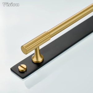 May include: A gold-toned metal handle with a black rectangular base. The handle has a cylindrical design with ridged detailing and a matching screw. The word "Vision" is in the top left corner. This hardware is suitable for cabinets, drawers, or doors.