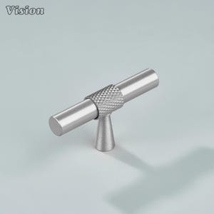May include: A silver-colored cabinet pull with a textured center section and cylindrical ends. The pull is mounted on a small, cone-shaped base. The word "Vision" is in the upper left corner.