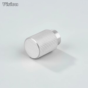 May include: A cylindrical, silver-coloured knob with a ridged body and a flat, circular top. The word "Vision" is in the upper left corner. The knob is likely a furniture or cabinet hardware component.