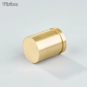 May include: A cylindrical brass object with a brushed finish. The object has a flat, circular end and a slightly raised ring near the other end. The word "Vision" is in the upper left corner.