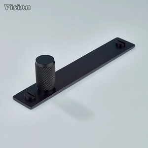 May include: A black metal cabinet pull with a textured cylindrical handle and a rectangular base. Two screws secure the base. The word "Vision" is in the upper left corner.