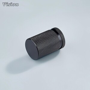 May include: A black cylindrical cabinet knob with a textured, diamond-patterned surface. The knob has a flat, circular end and a slightly raised, ridged edge on the other end. The word "Vision" is in the upper left corner.