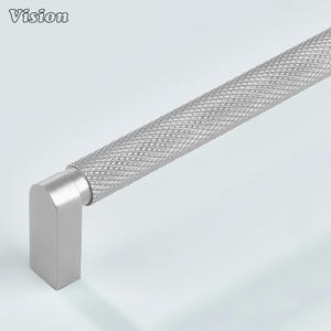 May include: A silver cabinet pull with a diamond-patterned handle and a rectangular end. The word "Vision" is in the upper left corner. The hardware is made of metal.