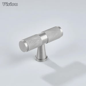 May include: A silver-colored cabinet knob with a textured, diamond-patterned handle. The knob has a cylindrical shape with a flat end and a conical base. The word "Vision" is in the top left corner.