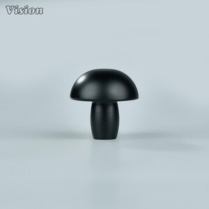 Op de afbeelding: Een zwart, paddenstoelvormig decoratief object. Het object heeft een afgeronde kap en een cilindrische steel. Het woord "Vision" staat in de linkerbovenhoek. Het object staat tegen een lichtgrijze achtergrond.
