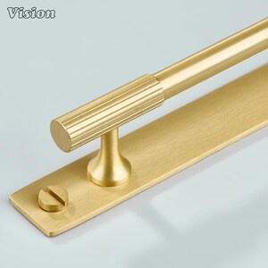 May include: A close-up shot of a gold-coloured cabinet pull. The cylindrical handle has a ribbed texture and is attached to a rectangular backplate. A screw is visible near the base. The word "Vision" is in the top left corner. The pull is likely for a cabinet or drawer.