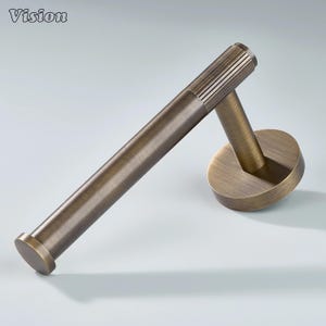 May include: A bronze-toned toilet paper holder with a cylindrical bar and a circular base. The bar has a ribbed texture on the end. The Vision logo is in the top left corner.