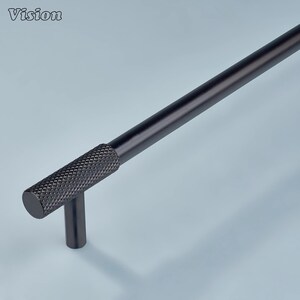 May include: A black cabinet pull with a textured grip and a cylindrical design. The word "Vision" is in the upper left corner. The pull is made of metal and has a matte finish.