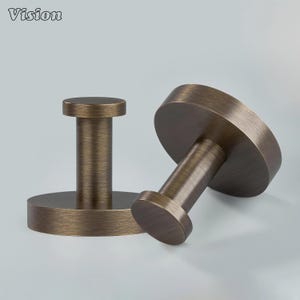May include: Two bronze-colored metal wall hooks. Each hook has a circular base and a cylindrical post topped with a smaller circular head. The hooks are designed for hanging items. The word "Vision" is in the top left corner.