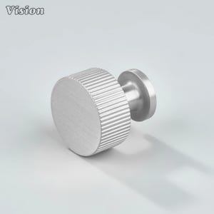 May include: A brushed metal cabinet knob with a circular, ridged grip and a small, round base. The word "Vision" is in the upper left corner. The knob is silver and appears to be made of stainless steel.