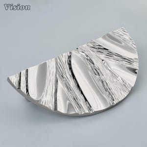 Puede incluir: Un tirador de mueble semicircular con acabado en cromo pulido. La superficie presenta un diseño texturizado y ondulado que imita la apariencia de agua corriente o vetas de madera orgánica, creando un aspecto metálico reflectante y brillante.