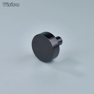Op de afbeelding: Een matzwarte kastknop met een cilindrisch lichaam en een korte, afgeronde steel. Het woord "Vision" staat in de linkerbovenhoek. De knop is ontworpen voor meubelbeslag en heeft een moderne, minimalistische uitstraling.