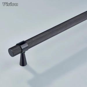 Può includere: Maniglia nera per mobili con un design a trama diamantata. L'hardware presenta una maniglia cilindrica e una base conica. La parola "Vision" è nell'angolo in alto a sinistra.