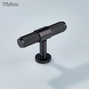 Op de afbeelding: Een zwarte kastgreep met een handvat met diamantpatroon. De T-vormige greep heeft een cilindrisch handvat en een cirkelvormige basis. Het woord "Vision" staat in de linkerbovenhoek.