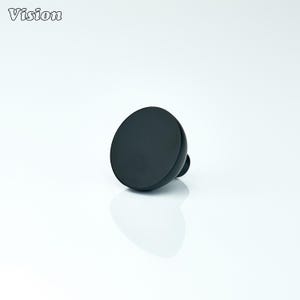 Puede incluir: Un pomo de armario negro y circular con un pequeño vástago redondeado. El pomo tiene un acabado liso y mate y está sobre un fondo blanco. La palabra "Vision" está en la esquina superior izquierda.