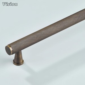 Op de afbeelding: Bronzen kastgreep met een textuur met diamantpatroon. Het Vision-logo staat in de linkerbovenhoek. De handgreep heeft een cilindrische vorm met een afgerond uiteinde en een conische basis.