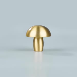 May include: A gold-colored mushroom-shaped cabinet knob. The knob has a rounded top and a cylindrical stem. The mushroom knob is made of metal and has a brushed finish. The knob is designed for use on cabinets, drawers, or furniture.